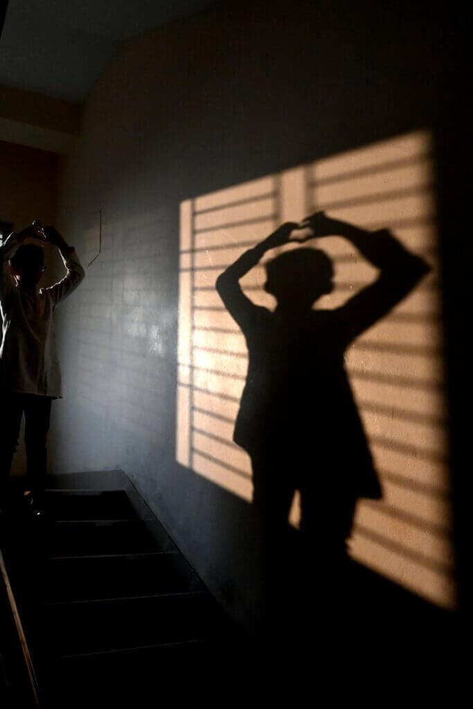 A person creates a silhouette on a stairway with dramatic shadows from a window.